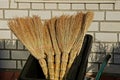 A pile of brown brooms near a brick wall