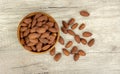 A pile brown seeds of Almond nut in wooden bowl and spill off on wooden table, top view angle of shooting with copy space