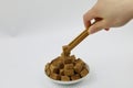 A pile of brown sugar cubes on a white plate woman hand hold wooden tweezers on white background Royalty Free Stock Photo