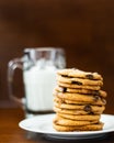 A pile of chocolate chip cookies on a white plant with a glass of milk in the background Royalty Free Stock Photo