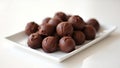 A pile of chocolate truffles on a white square plate displayed on a white surface in soft lighting Royalty Free Stock Photo