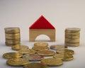 Pile of coins and a model of a house on a light background. Royalty Free Stock Photo
