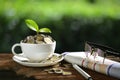 Pile of coins and young plant on top in coffee cup with newspapers and glasses showing concept of of business Royalty Free Stock Photo