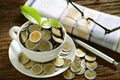 Pile of coins and young plant on top in coffee cup with newspapers Royalty Free Stock Photo