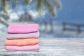 Pile of colorful knitted cozy warm cashmere sweaters on wooden table against blurred abstract snowy landscape xmas background.