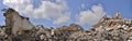 A pile of concrete gray debris of a destroyed building with a huge beam in the foreground against a blue sky with clouds