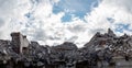 A pile of concrete gray debris of a destroyed building with a huge beam in the foreground against a blue sky with clouds