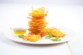 pile of crispy jalebi on white plate, golden syrup dripping