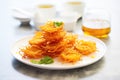 pile of crispy jalebi on white plate, golden syrup dripping