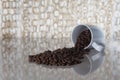 Pile of dark roasted coffee beans falling out of a white cup on a sunlight counter Royalty Free Stock Photo