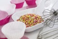 Pile of decorative sugar stars in a bowl with whisk sticks for eggs and white and pink paper molds for muffins