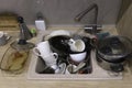 Pile of dirty dishes like plates, cups pot and cutlery in the white kitchen in the light beige granite sink Royalty Free Stock Photo
