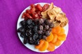 A pile of dried fruits apples, prunes, apricots, pears, cranberries on a white plate on a purple background. Antioxidant mix