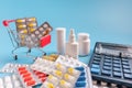 Pile of drugs and medicine bottles, calculator and shopping trolley cart filled pills. selective focus Royalty Free Stock Photo