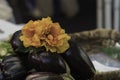 Pile of eggplant at the market decorated with a group of orange fabric flowers