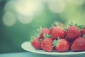 Pile of fresh red strawberries on a white plate with a blurred green background outdoors Royalty Free Stock Photo