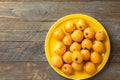 Pile of freshly picked ripe juicy bright orange loquat fruits on bright yellow plate on vintage wooden table top view