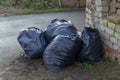 Pile of garbage bags. Lots black garbage bag with street and old brick wall background.