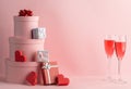 Pile of gift boxes, red hearts and glasses of prosecco on pink background