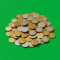 A pile of gold and silver coins scattered on a solid green background. The coins Royalty Free Stock Photo