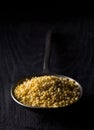 Pile of golden millet, a gluten free grain seed, in metal spoon on dark wood background