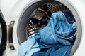 Pile of jeans in the drum of open washing machine in laundry room.