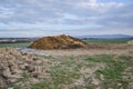 Pile of manure in the countryside with blue sky. Heap of dung in field on the farm yard with village in background