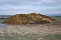 Pile of manure in the countryside with blue sky. Heap of dung in field on the farm yard with village in background