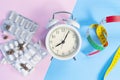 Pile of medical pills and a multi-colored centimeter with a white classic alarm clock on a pink and light blue background Royalty Free Stock Photo