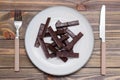 A pile of molded pieces of chocolate on a plate and cutlery on a wooden table. The concept of eating sweet time