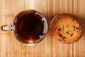 A pile of oatmeal cookies with chocolate chips and a mug of fragrant black hot tea in on a bamboo substrate, on a dark background Royalty Free Stock Photo