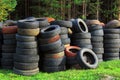 A pile of old car tires lies on the grass against the background of the forest. Ecology concept Royalty Free Stock Photo