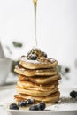 Pile of pancakes with blueberry on the top, maple leaf is pouring on it.