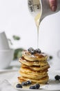 Pile of pancakes with blueberry on the top, maple leaf is pouring on it by a woman`s hand.