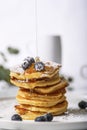 Pile of pancakes with blueberry on the top, maple syrup is pouring on it.