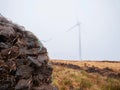 Pile of peat fossil fuel in foreground, wind power turbine in a fog in the background. Old and new source of energy. Ecology Royalty Free Stock Photo