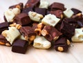 Pile of pieces of milk chocolate, white chocolate and dark chocolate with hazelnuts on a wooden background