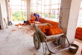 Pile of red blocks in wheelbarrow, worker builds wall with bricks and mortar, building site Royalty Free Stock Photo