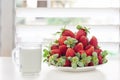 A pile of red fresh strawberries on a white plate and a cup of milk