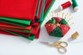 Pile of red and green fabrics, pincushion, scissors, thimble and spools of thread on white background