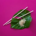 Pile of rice with chopsticks and leaf on purple background. Top view
