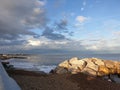 Pile of rocks on the beach under blue cloudy sky seen from walkway on the shore