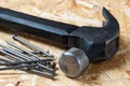 A pile of steel nails and a metal hammer lying on chip board. Blurred background Royalty Free Stock Photo