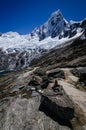 Pile of stones in the foreground with high snowy mountain of Taulliraju in the background, on the trekking of the santa cruz