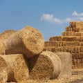 A pile of straw rolls and rectangular sheaves of straw, against a sky