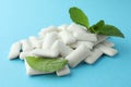 Pile of tasty white chewing gums and mint leaves on light blue background, closeup