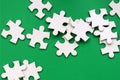 A pile of uncombed elements of a white jigsaw puzzle lies on the background of a green surface. Texture photo with copy space for