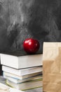 Pile of various books, red apple and package of lunch on dark ba Royalty Free Stock Photo