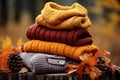 Pile of warm knitted clothes with autumn leaves on blurry rustic background