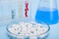 A pile of white medical pills in petri dish against labware with capsules and blue solution, isolated on blue background